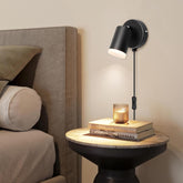 Black wall lamp on a nightstand next to a bed with books and a candle.